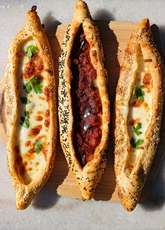 three pieces of bread with meat and cheese in them sitting on a cutting board next to each other