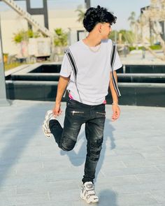 a young man with black hair and white shirt is walking down the street holding a skateboard