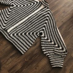 a black and white knitted sweater laying on top of a wooden floor next to a laptop computer