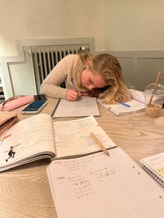 a woman is sitting at a table with notebooks and pens in front of her