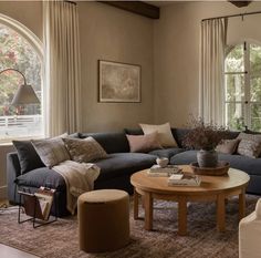 a living room filled with lots of furniture next to two large windows and a rug on the floor