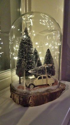 a snow globe with a car and trees in it on top of a table next to a window