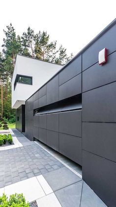 an exterior view of a modern house with black and white sidings, trees, and landscaping