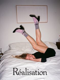 a woman laying on top of a bed with her legs up and feet in the air