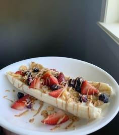 a white plate topped with bananas and strawberries on top of a window sill