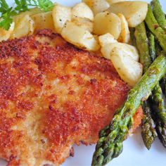 a white plate topped with fish and asparagus next to potato wedged potatoes