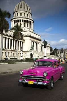 an old pink car is parked in front of a large building with a dome on top