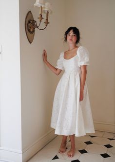 a woman in a white dress standing next to a wall with a light on it