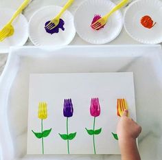 a child's hand is holding a paper plate with flowers on it and three plates behind them