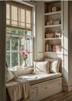 a window seat with pillows and flowers on it in front of a bookshelf