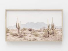 a desert scene with cactus trees and mountains in the background, framed in white paper