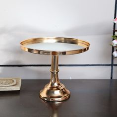 a gold plate sitting on top of a wooden table next to a vase with flowers