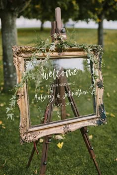 an easel with a sign that says welcome to the wedding and is decorated with greenery