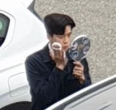 a man holding two mirrors in front of his face while standing next to a white car