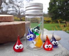 three glass vases with eyes are sitting on a table next to some rocks and trees