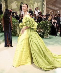 a woman in a yellow gown standing on a white carpet with people taking pictures behind her