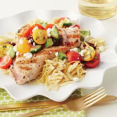 a white plate topped with chicken and veggies on top of pasta next to a glass of wine