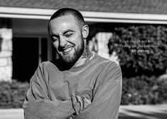 a black and white photo of a smiling man in front of a house with his arms crossed