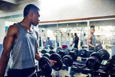 a man standing in front of a row of dumbbells with another man behind him