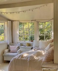 a bedroom with white bedding and pillows on the windowsills is lit by sunlight coming through the window panes