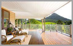 a porch with chairs and tables on it next to a wooden deck overlooking the mountains