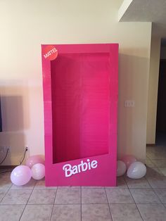 a pink box with the word barbie on it sitting in front of some white balloons