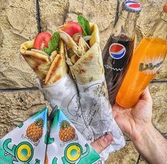 a person holding food in their hand next to a bottle of soda and an orange juice