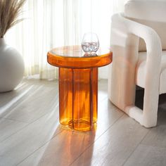 an orange table with two wine glasses on it next to a white chair and window