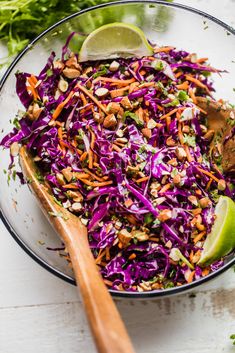 a glass bowl filled with coleslaw slaw and lime wedges next to a wooden spoon