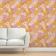 a white couch sitting in front of a wall with orange and pink flowers on it