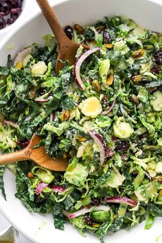 a white bowl filled with green salad and wooden spoons next to cranberry sauce