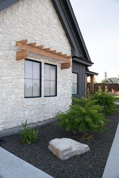 a stone bench sitting in front of a white brick building next to a green plant