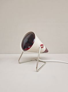 a white table lamp with a red light on it's side and a silver base