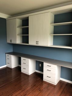 an empty room with blue walls and white cabinets on the wall, hardwood flooring