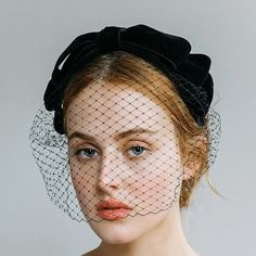 a woman with a veil on her head wearing a black dress and tulle hat