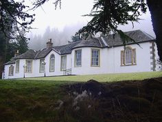 a large white house sitting on top of a lush green hillside next to a forest