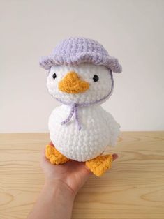 a hand holding a small white crocheted duck with a purple hat on it's head