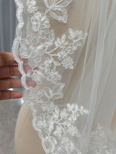 the back of a wedding dress with white flowers on it, being held up by someone's hand