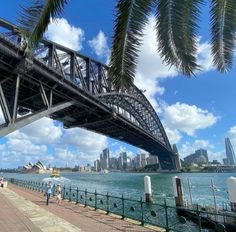 people are walking along the water under a bridge