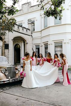 a group of women standing next to each other in front of a white car with pink flowers