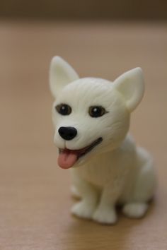 a small white dog figurine sitting on top of a wooden table with its tongue out