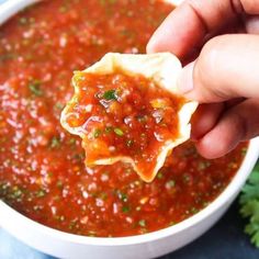 a hand holding a tortilla chip over a bowl of salsa