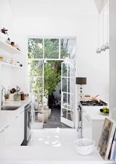 a white kitchen with open glass doors leading to the outside