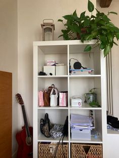 a white book shelf filled with lots of books and purses next to a green plant