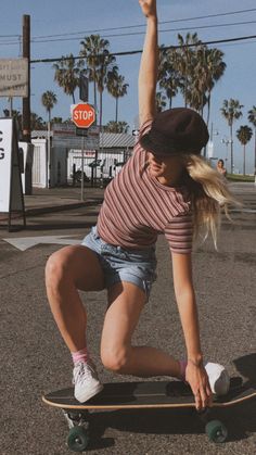 a woman riding a skateboard down the middle of a street with palm trees in the background