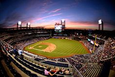 a baseball stadium filled with lots of people sitting on the bleachers at sunset