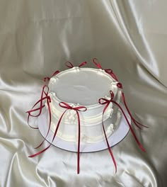 a white cake with red ribbon around it sitting on a satin tablecloth covered surface