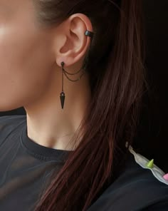 a woman with long hair wearing black earrings and a chain around her ear is looking away from the camera