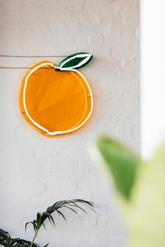 an orange painted on the side of a white wall next to a potted plant