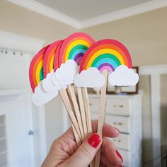 a person holding up some paper clouds and rainbows on toothpicks in their hand